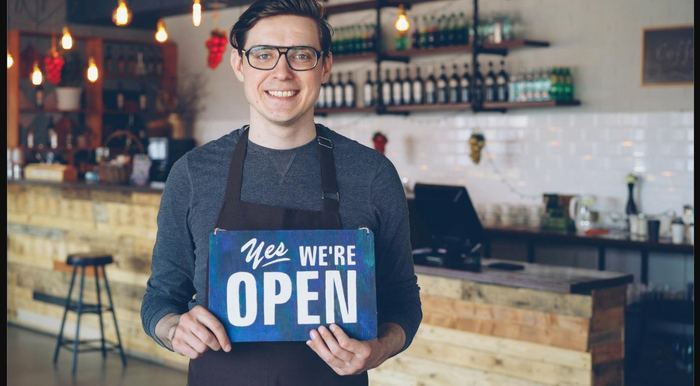 A small business owner holding an open sign in his shop